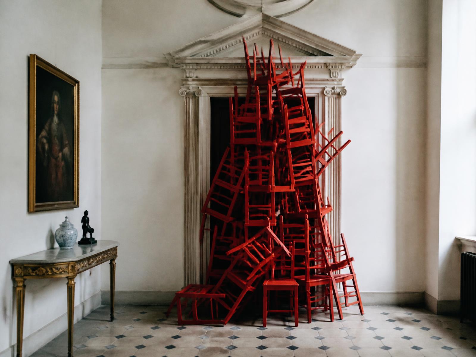 A precarious stack of red chairs blocking a doorway in a Palladian country house