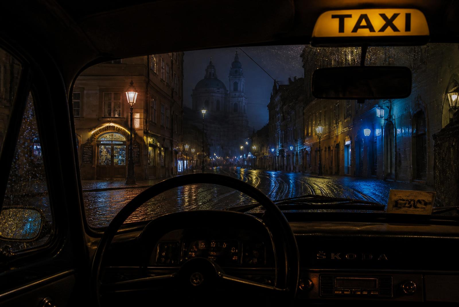 View through the windscreen of a Prague taxi on wet cobbles at night, yellow roof lamp lit